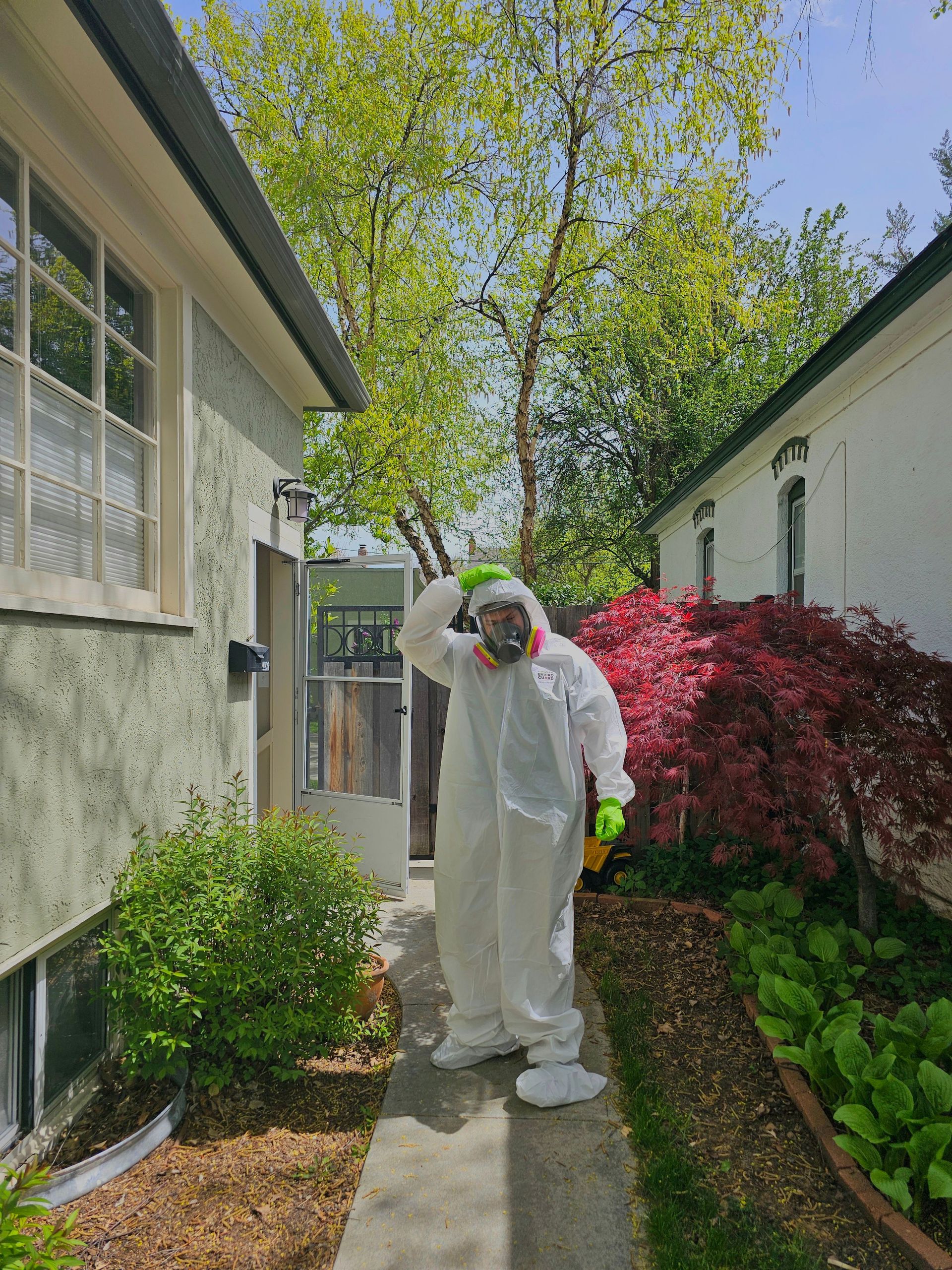 A person in protective gear and gas mask standing in a lush garden on a sunny day.